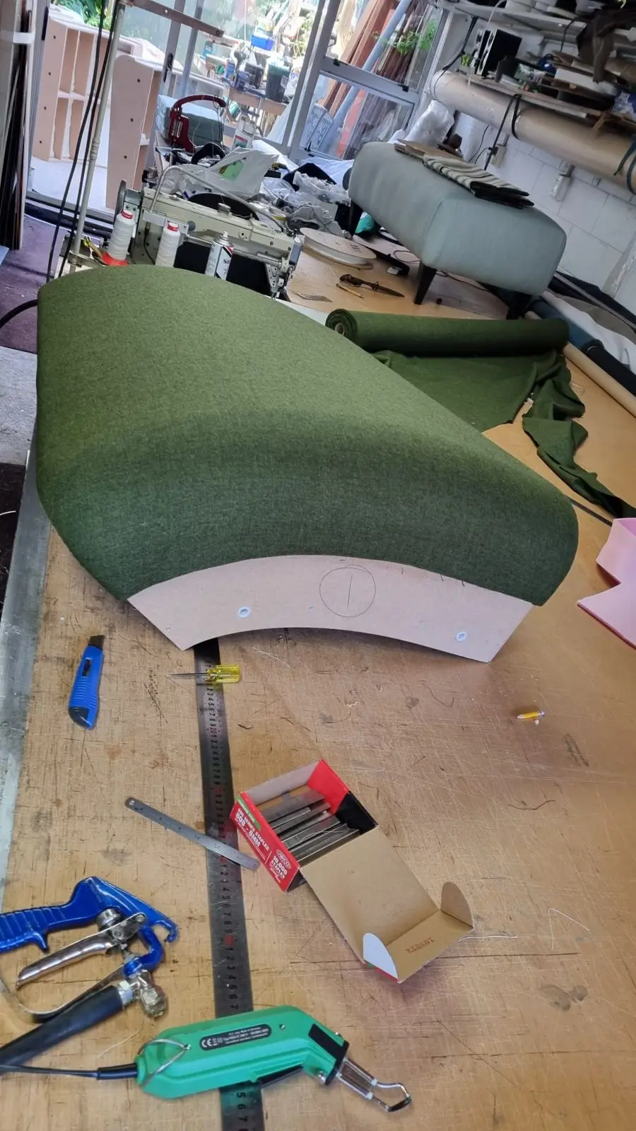 Curved seat back upholstered in green fabric in the workshop